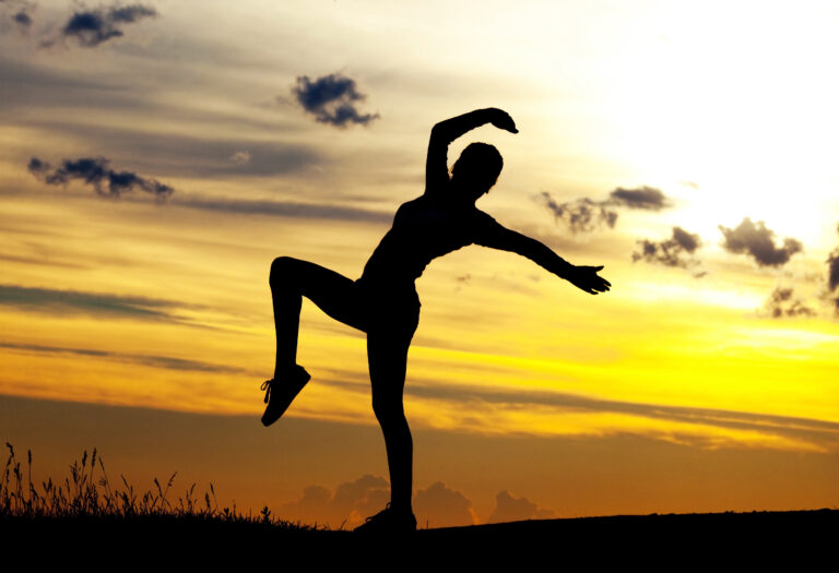 Silhouette of woman moving gracefully in front of sunset